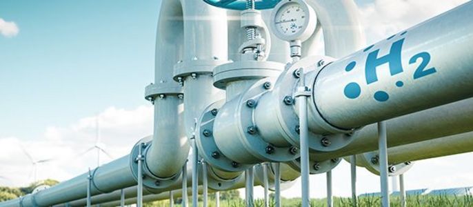 Eine Reihe weißer Rohre mit der Aufschrift "H2" und einem blauen Ventil vor einem Hintergrund aus grünem Gras und einem klaren Himmel.