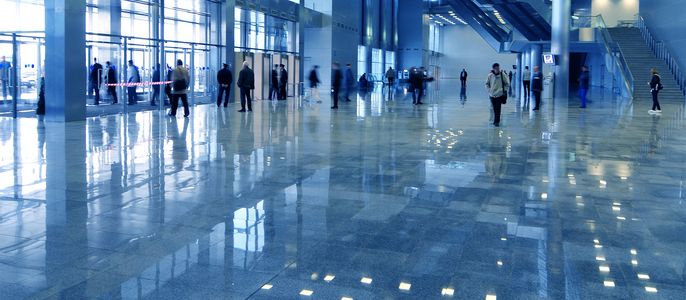 Die Lobby eines modernen Gebäudes mit laufenden Menschen, einem reflektierenden Boden und Glastüren.