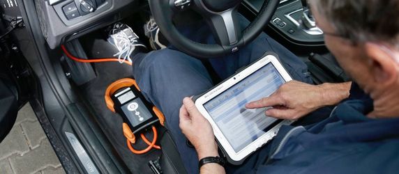 Ein Mann in einem Auto, der ein Tablet benutzt, um etwas auf dem Armaturenbrett zu überprüfen.