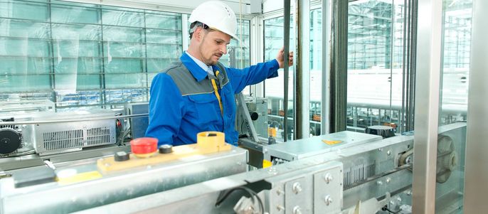 Ein Mann in blauer Uniform und weißem Schutzhelm inspiziert Maschinen in einer modernen Industrieumgebung.