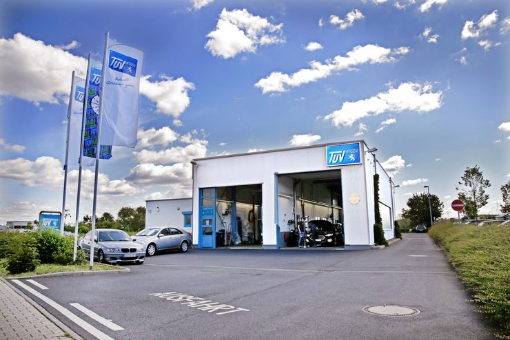 Eine moderne Autotankstelle mit weißem Gebäude, blauem Schriftzug und einigen draußen geparkten Autos.