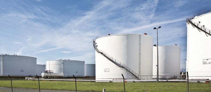 Mehrere große weiße zylindrische Lagertanks, einige mit Leitern, auf einer offenen Fläche mit einem Zaun im Vordergrund.