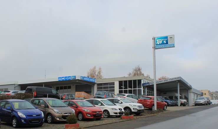 Ein Autohaus mit verschiedenen Autos, die draußen geparkt sind, ein Schild mit der Aufschrift "TUEV Service-Center".