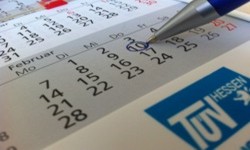 Ein Kalender mit einem blau eingekreisten Datum und dem Logo des TÜV Hessen unten rechts.